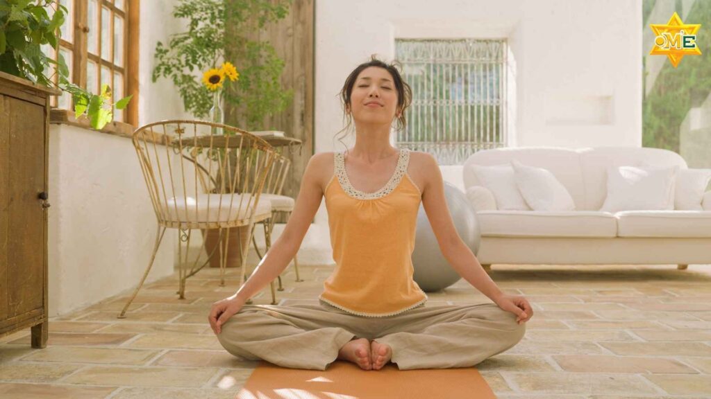 Người phụ nữ đang ngồi thiền tư thế hoa sen trên thảm yoga trong phòng khách tràn ngập ánh sáng tự nhiên.